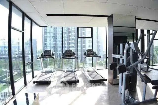 Modern gym with treadmills and exercise equipment in a high-rise building with city views.