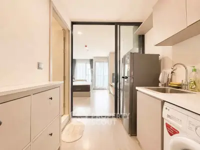 Modern apartment kitchen with sleek appliances and view into cozy bedroom