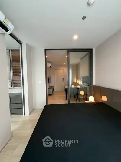 Modern bedroom with sleek design and glass partition leading to living area, featuring ambient lighting.