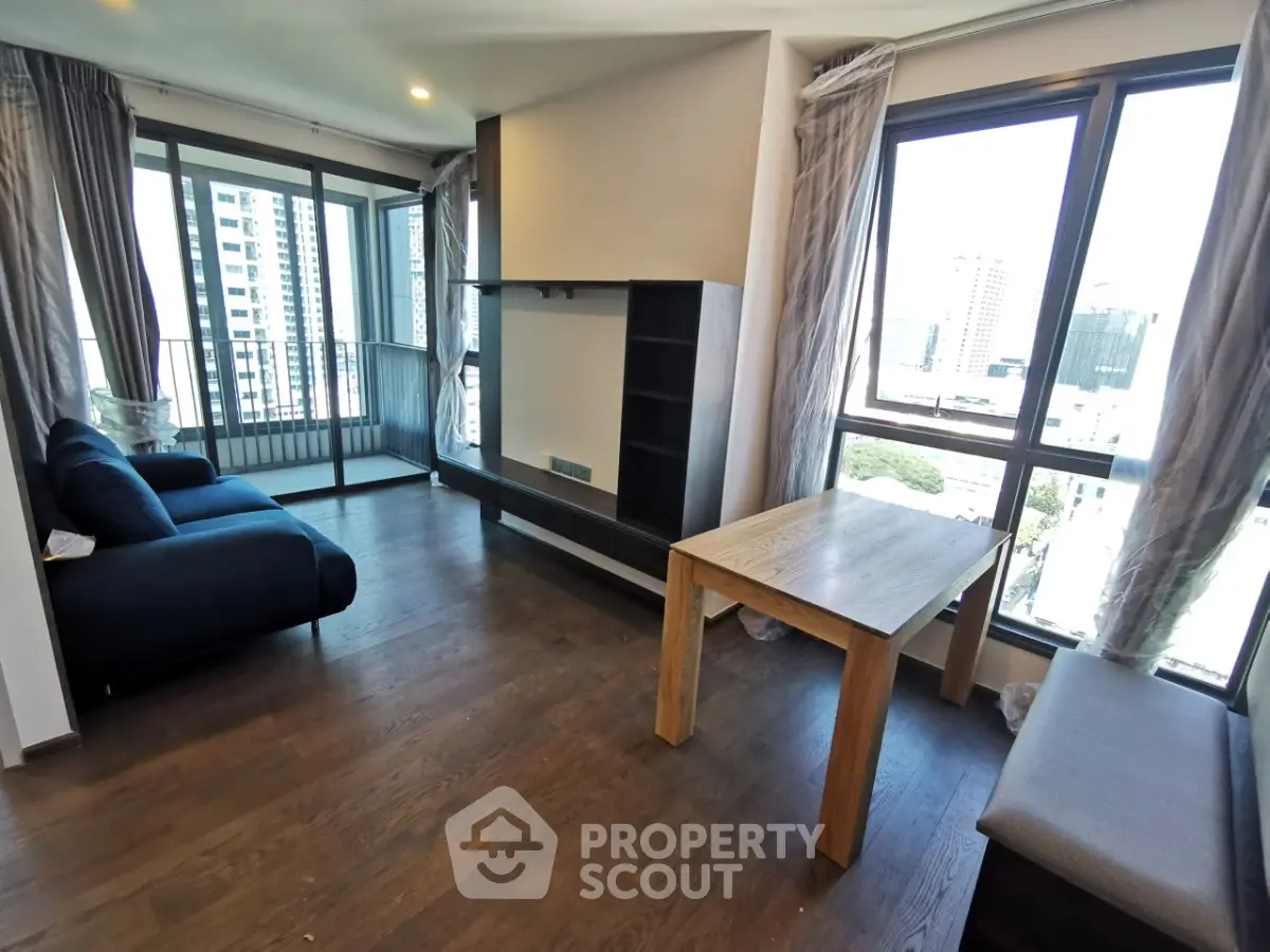 Spacious modern living room with large windows and city view, featuring stylish furniture and elegant wooden flooring.