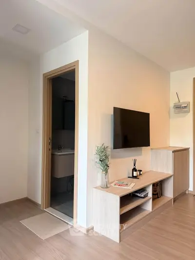 Modern living room with wall-mounted TV and sleek wooden furniture, adjacent to a compact bathroom.