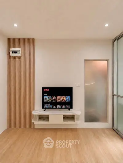 Modern living room with wooden flooring, TV setup, and stylish wall paneling.