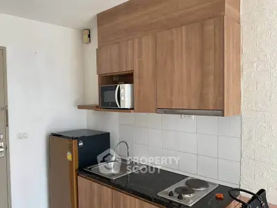 Modern compact kitchen with wooden cabinets, microwave, and mini fridge in a cozy apartment.