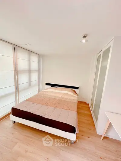 Modern minimalist bedroom with wooden flooring and ample natural light.