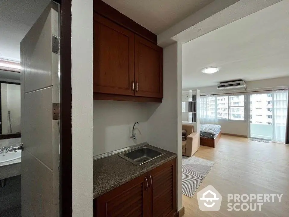 Spacious studio apartment with modern kitchenette and large windows offering city views.