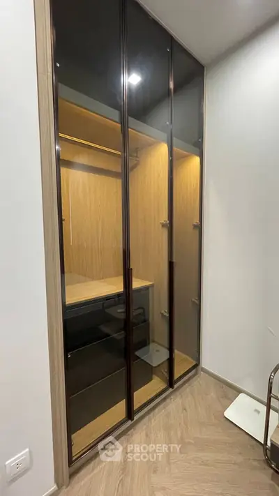 Modern walk-in closet with sleek glass doors and wooden interior design.