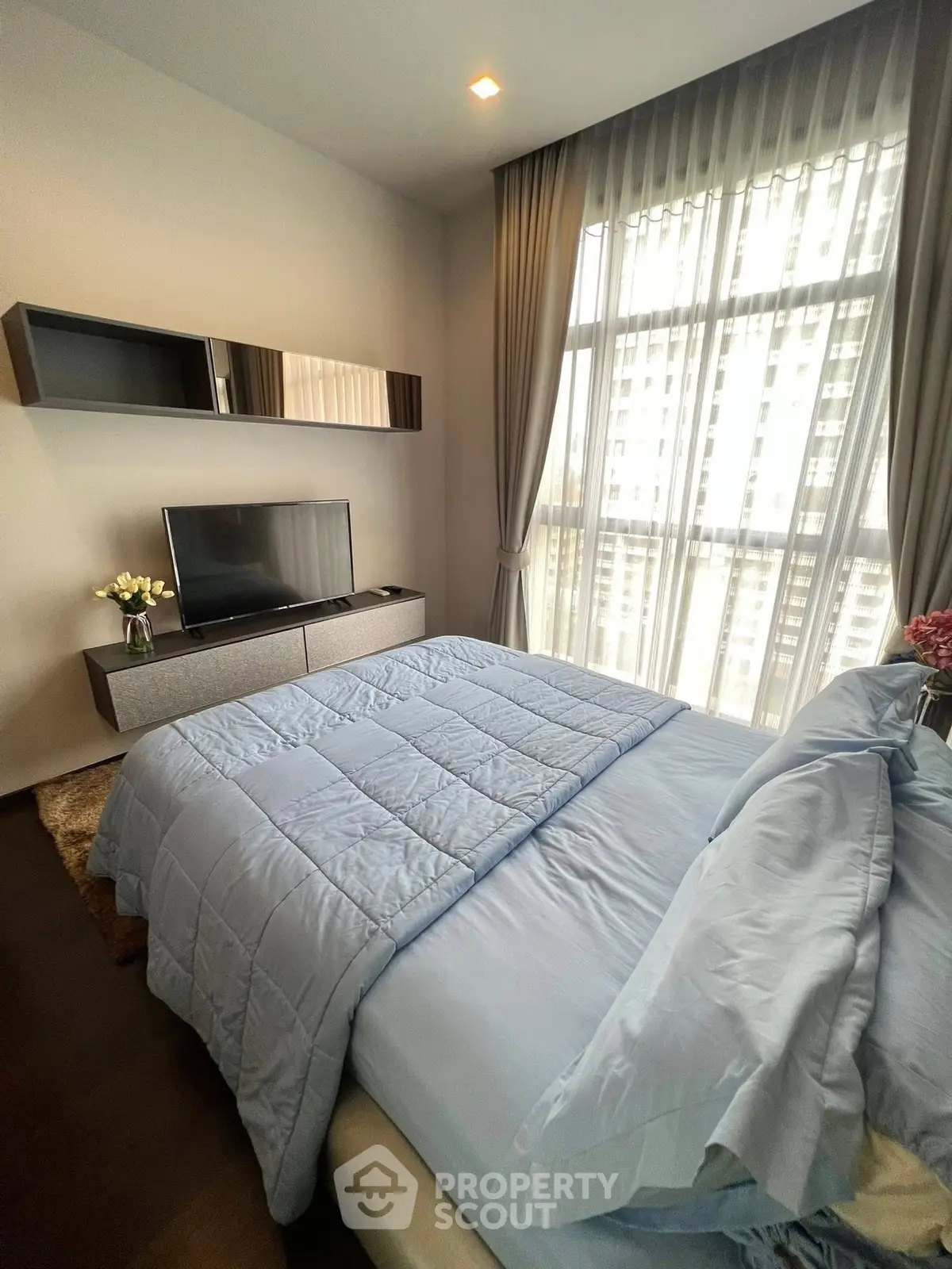 Modern bedroom with large window and stylish decor in a high-rise apartment.