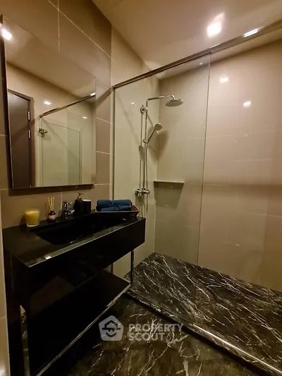 Luxurious modern bathroom with sleek black marble and glass shower enclosure.