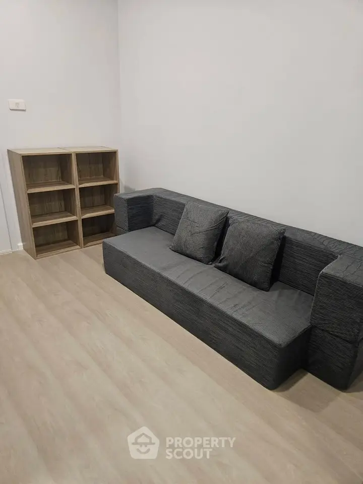 Modern minimalist living room with sleek gray sofa and wooden shelving unit.