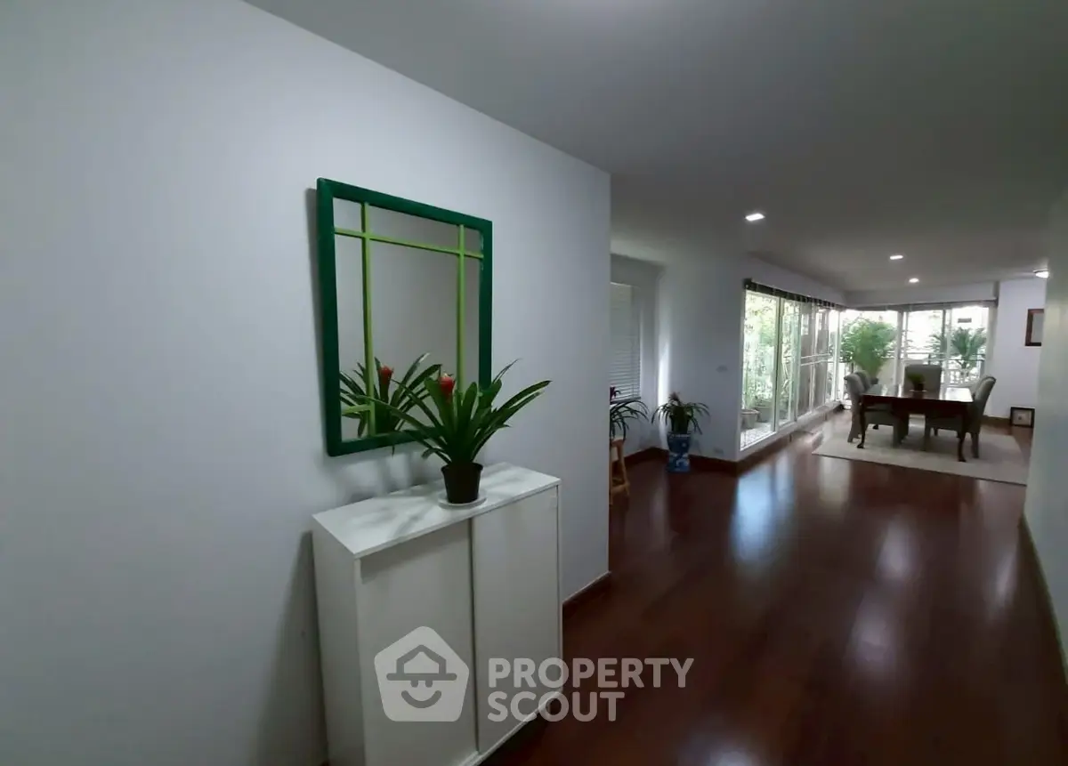Spacious hallway with wooden flooring and modern decor leading to a bright living area with garden view.