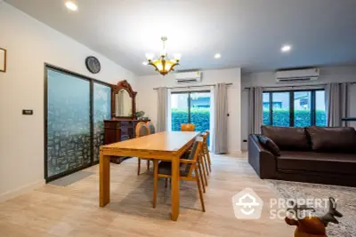 Spacious living room with elegant wooden dining table, cozy leather sofa, and large sliding glass doors leading to a lush garden view.