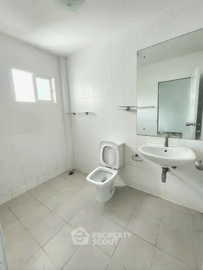 Spacious white-tiled bathroom with modern fixtures and natural light.