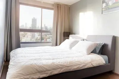 Modern bedroom with large window offering stunning city view, elegant decor, and cozy ambiance.