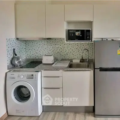 Modern compact kitchen with washing machine, microwave, and fridge in sleek design.