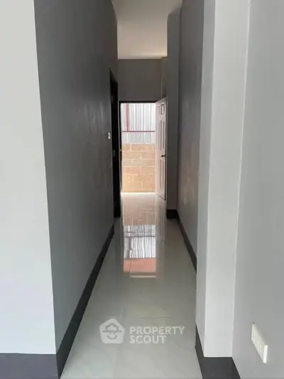 Sleek modern hallway with glossy tiled floors and open door leading to outdoor area.
