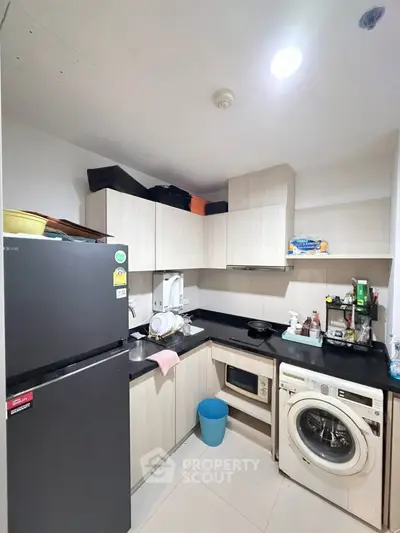 Modern compact kitchen with washing machine and microwave in sleek apartment.