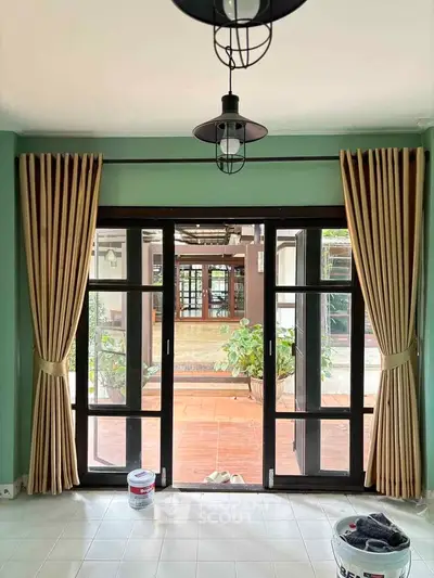 Charming interior view with large glass doors opening to a cozy patio, featuring elegant curtains and modern lighting.