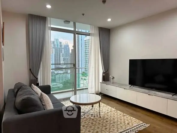 Modern living room with large TV and city view from balcony, featuring sleek furniture and elegant decor.
