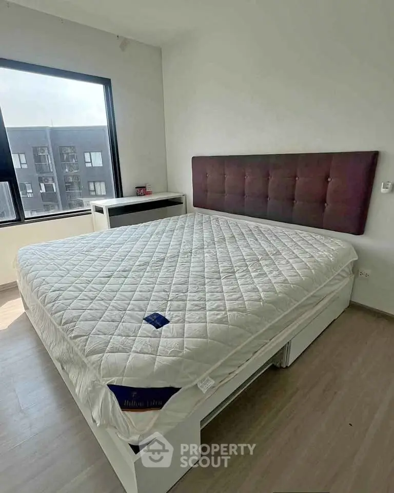 Spacious bedroom with large window and modern furnishings in a stylish apartment.
