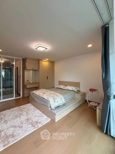 Modern bedroom with wooden flooring, cozy bed, and ample natural light from large windows.