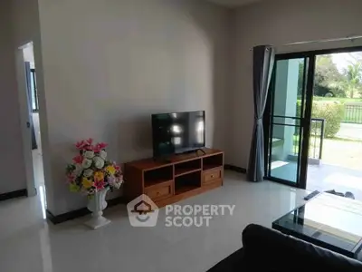 Spacious living room with modern decor and garden view, featuring a TV and elegant floral arrangement.