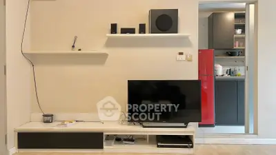 Modern living room with sleek TV setup and open kitchen view, featuring stylish shelves and red fridge.