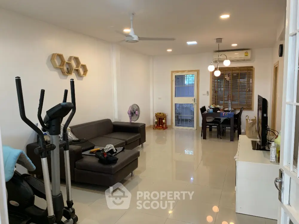 Spacious living room with glossy tiled flooring, modern lighting, and an open layout extending to a cozy dining area, perfect for entertaining and relaxation.
