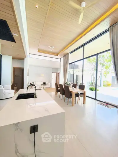 Luxurious open-plan living room with modern kitchen and dining area, featuring floor-to-ceiling windows and elegant decor.