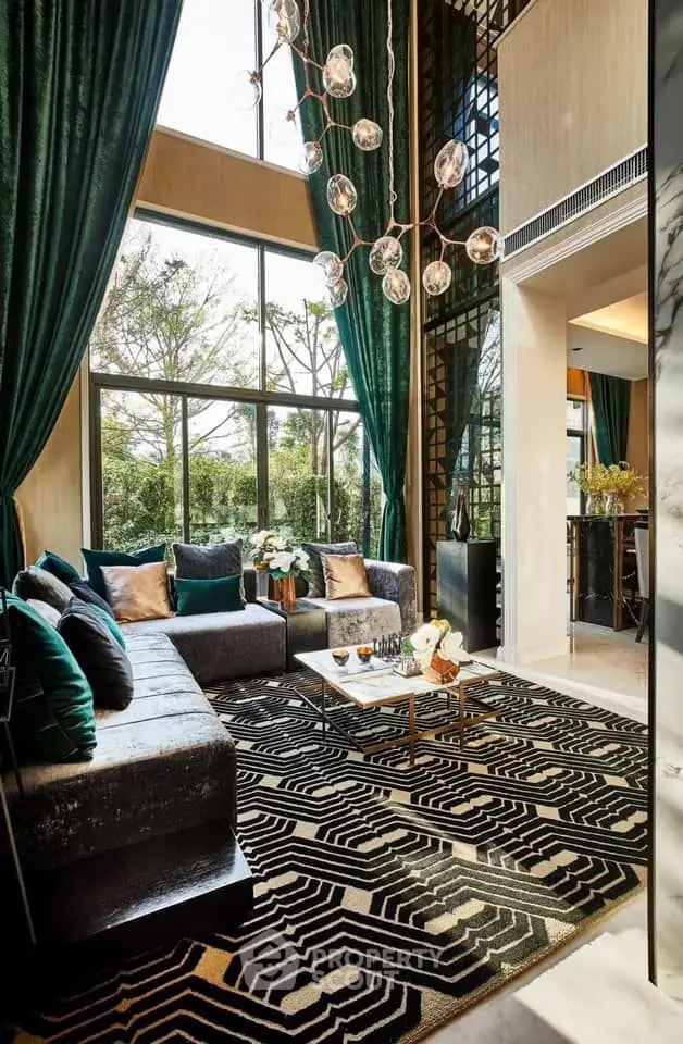 Luxurious living room with high ceilings, elegant chandelier, and large windows offering garden views.