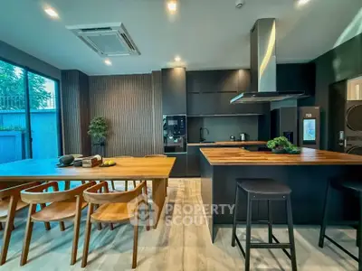 Modern kitchen with sleek black cabinets and wooden dining table, featuring open layout and stylish lighting.