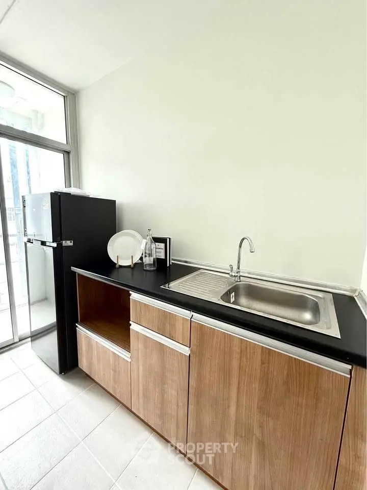 Modern kitchen with sleek cabinetry and stainless steel sink, featuring a compact fridge and ample natural light.