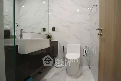 Modern bathroom with sleek fixtures and marble walls, featuring a contemporary sink and toilet.