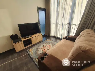 Cozy living room with plush sofa, modern entertainment unit, elegant drapery, and a classic area rug leading to a sunlit balcony.