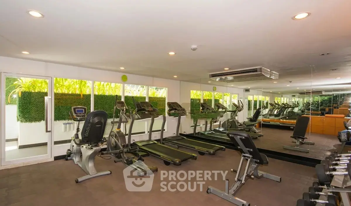 Spacious gym with modern equipment and mirrored walls in luxury apartment complex.