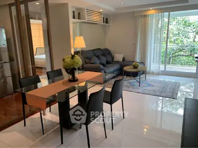 Modern living room with glass dining table and cozy seating area, featuring a view of lush greenery.