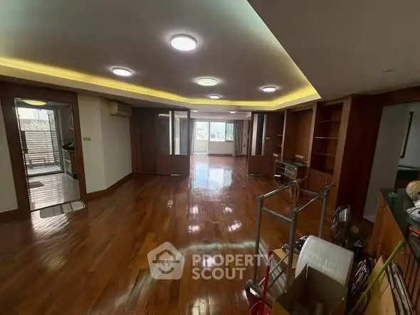 Spacious living room with wooden flooring and modern lighting in a well-lit apartment.