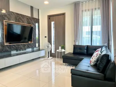 Modern living room with sleek black leather sofa and large wall-mounted TV, featuring elegant decor and natural light.