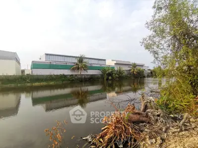 Industrial buildings by a serene riverside with lush greenery and clear skies.