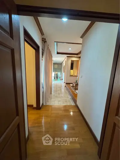 Spacious hallway leading to a bright living area with wooden flooring and elegant decor.