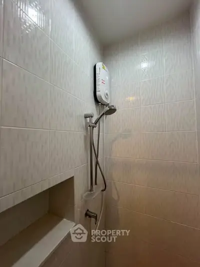 Compact bathroom shower area with modern water heater and tiled walls.