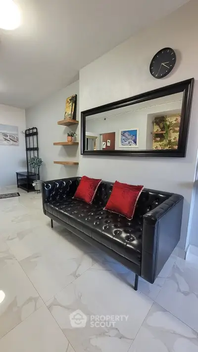 Modern living room with black leather sofa and red cushions, elegant decor and wall art.