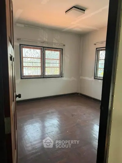 Spacious empty room with wooden floors and large windows, perfect for customization.