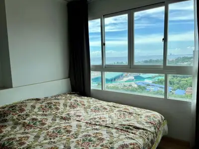 Cozy bedroom with large window offering stunning panoramic city and sea views.
