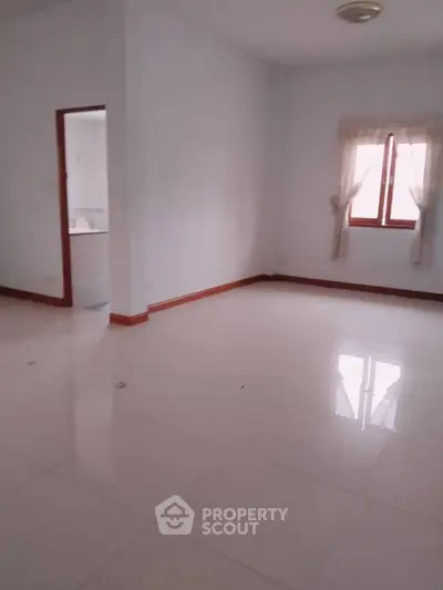 Spacious empty room with tiled flooring and natural light from window.