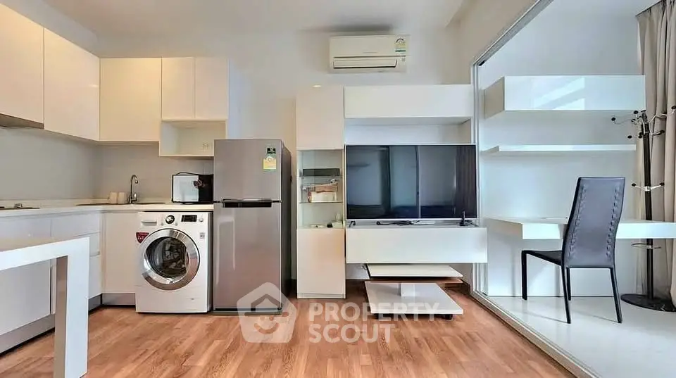 Modern open-plan living room with kitchen, featuring washing machine and sleek furniture.