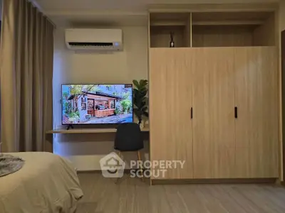 Modern bedroom with built-in wardrobe and wall-mounted TV, featuring sleek wooden finishes and air conditioning.