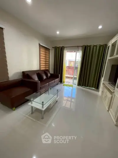 Modern living room with sleek furniture and glass coffee table, featuring large windows and elegant curtains.