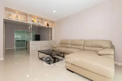 Spacious living room with modern beige leather sectional and sleek glass coffee table.
