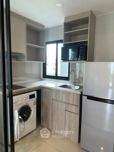 Modern kitchen with washing machine, microwave, and fridge in compact layout.