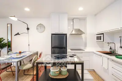 Modern kitchen with sleek white cabinets, dining area, and stylish lighting fixtures.